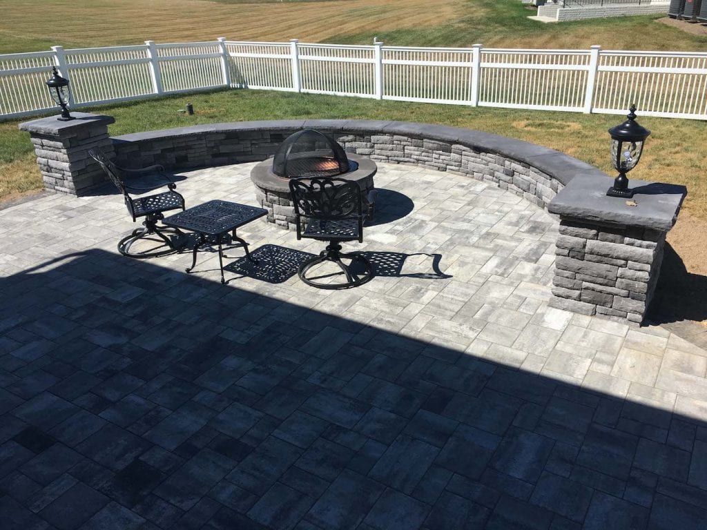 Gray patio with wall with black capstone and landscape lighting